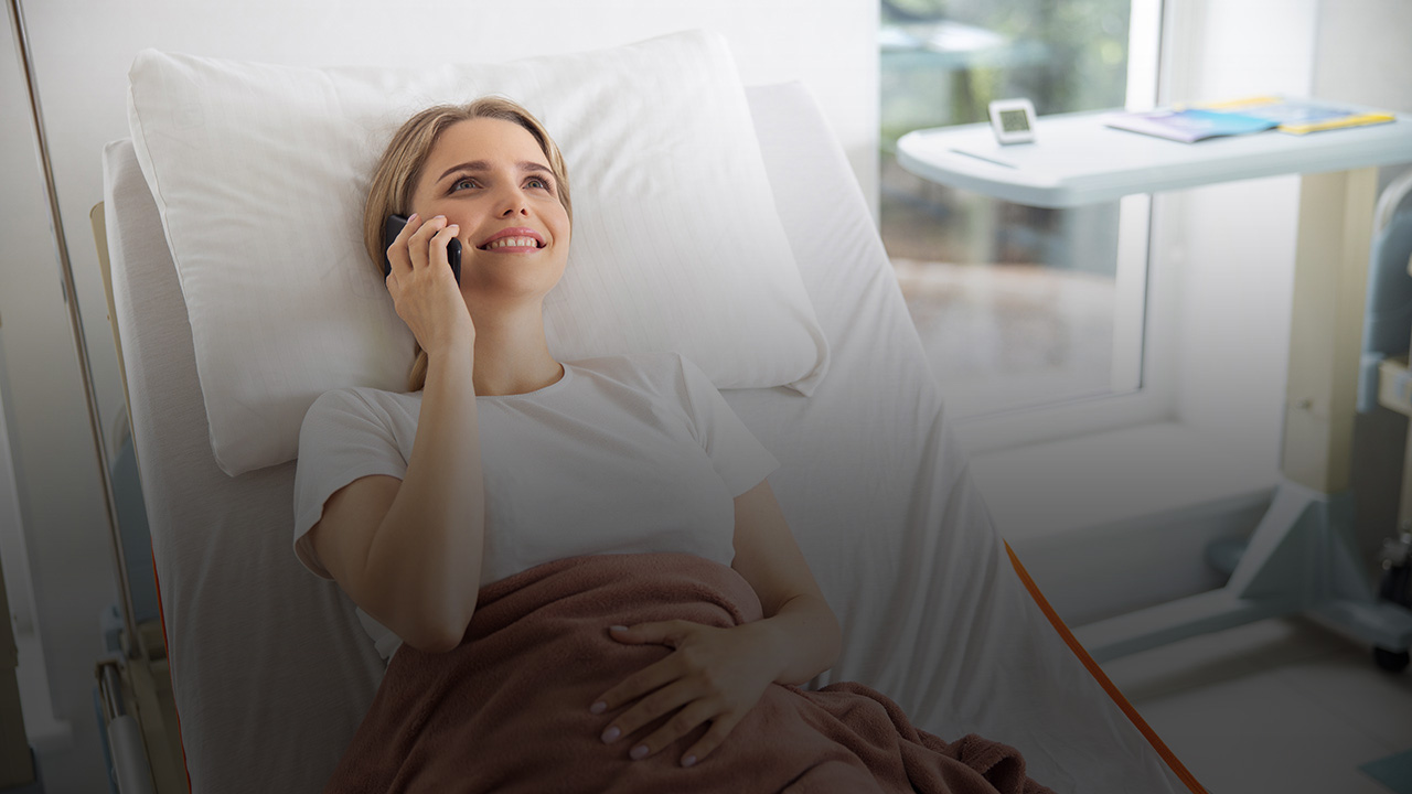 Eine Frau liegt in einem Krankenhausbett und telefoniert mit ihrem Mobiltelefon.